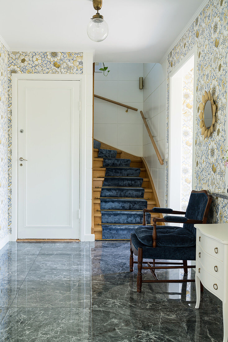 A cosy chair in front of a staircase in a hallway with floral wallpaper