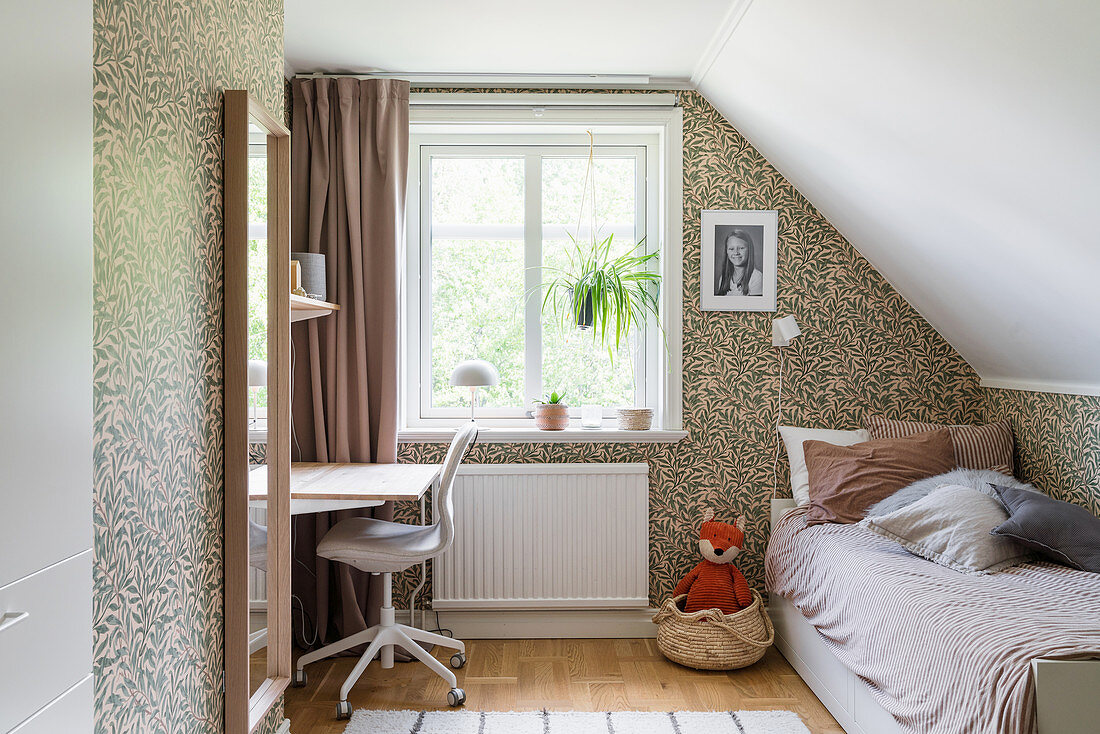 A bed and a desk in a girl's room with wallpaper in the attic