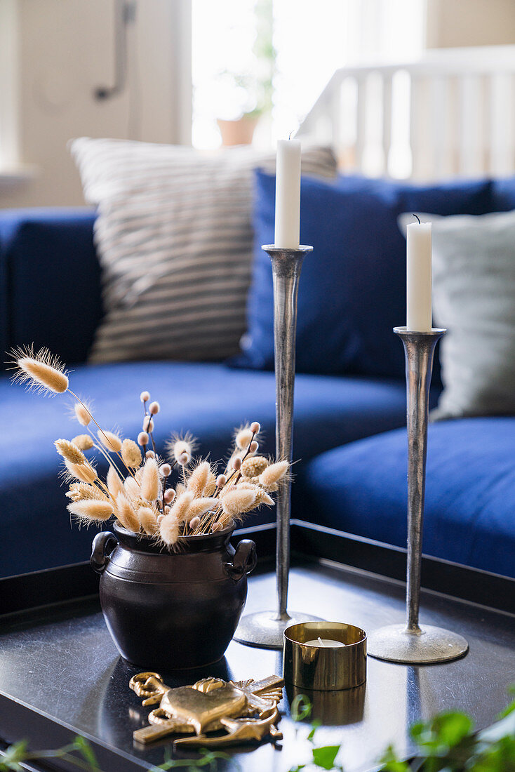 A candlestick and a vase with dried flowers on a coffee table