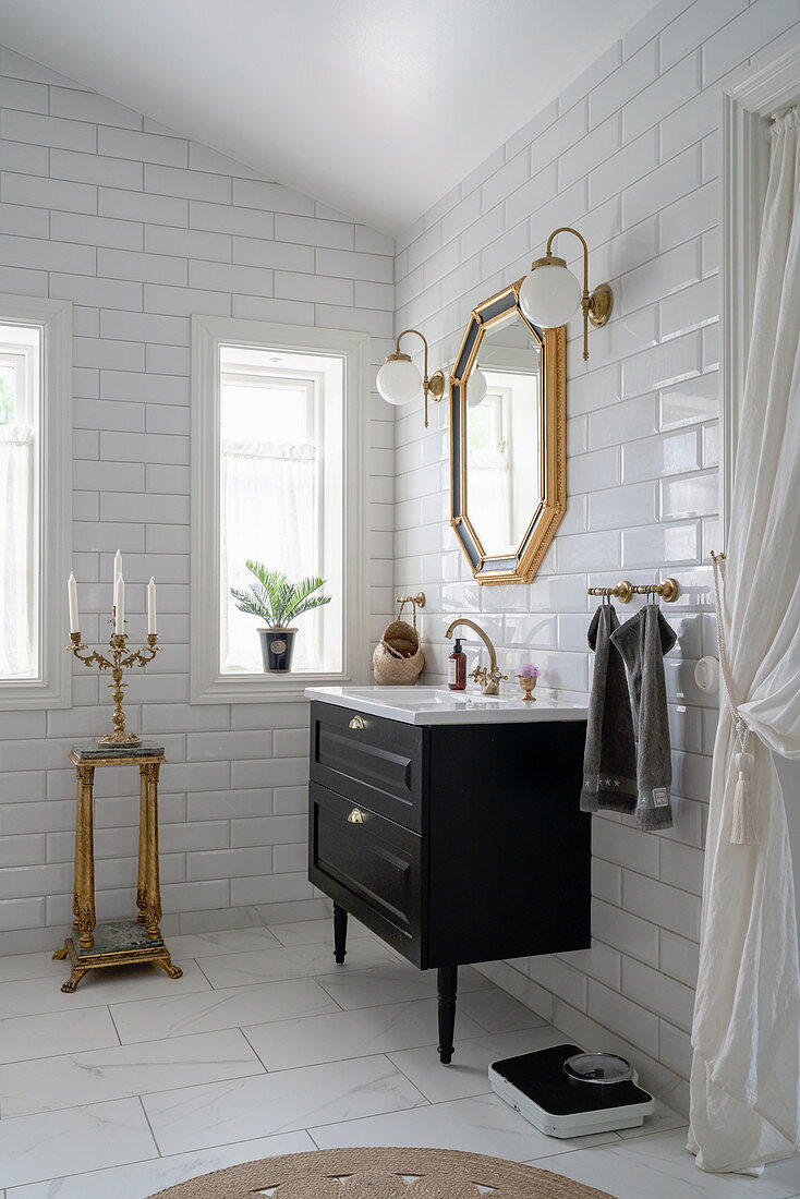 A washbasin and a gold-framed mirror in a bathroom with white subway tiles