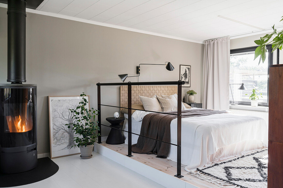 Doppelbett im Schlafbereich mit Eisengeländer als Raumteiler und Kaminofen