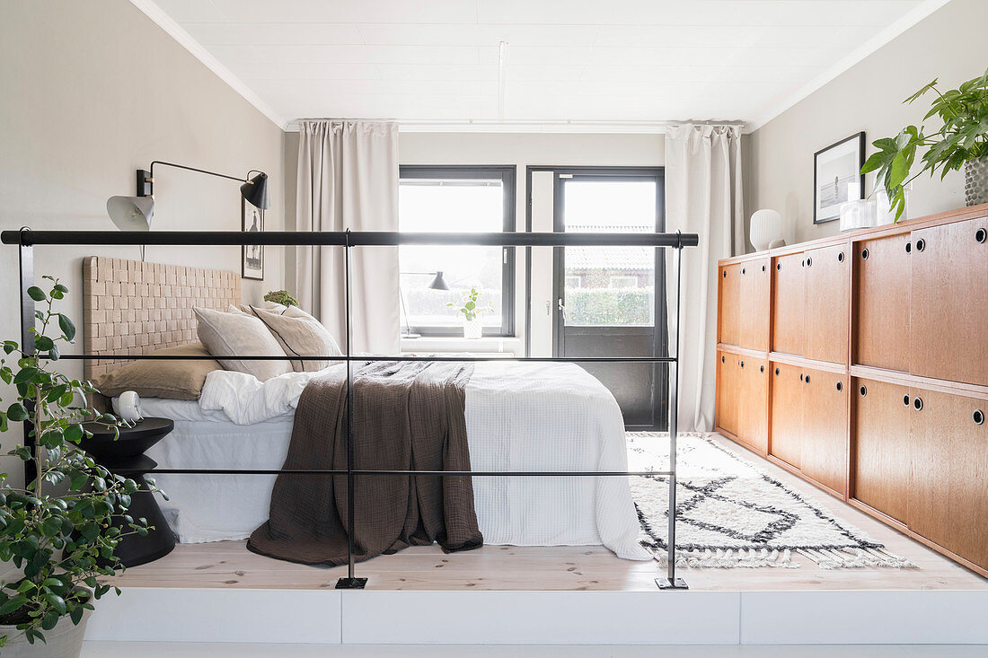 Doppelbett und halbhoher Schrank im Schlafbereich mit Eisengeländer als Raumteiler