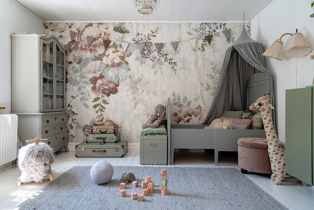 A bed with a curtain in front of a wall papered with floral wallpaper in a matt-coloured girl's room