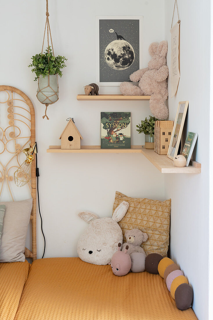 Soft toys on a bed below shelves in a corner of a bedroom