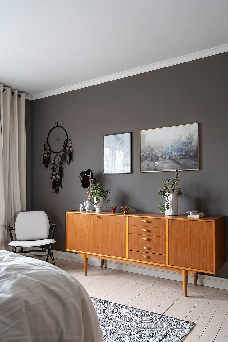 Armchair, dream catcher and sideboard in front of a dark wall in the bedroom