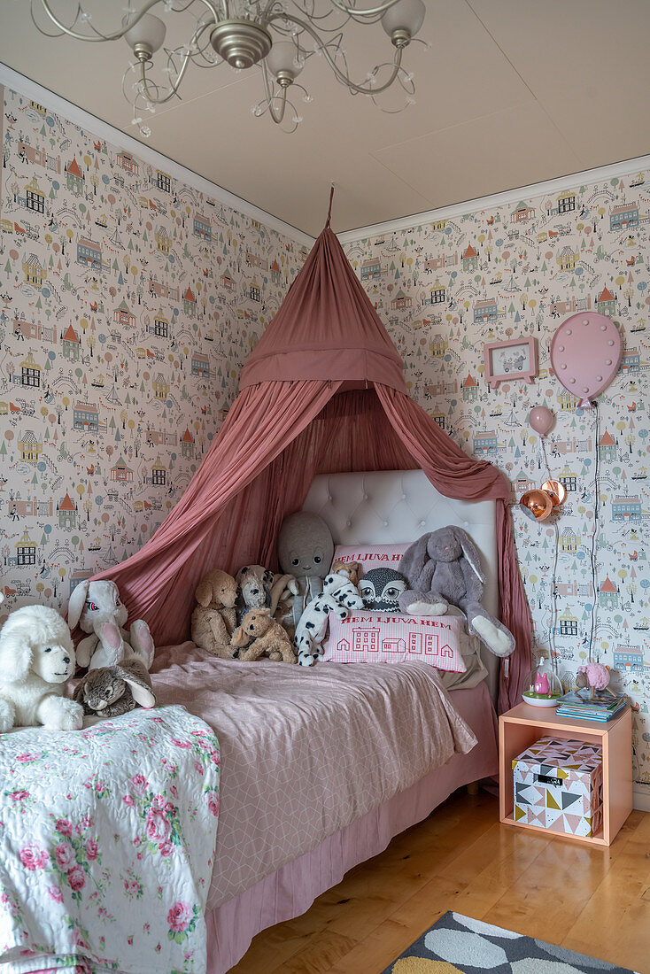Cuddly toys on a bed with a canopy in a girl's room with wallpaper