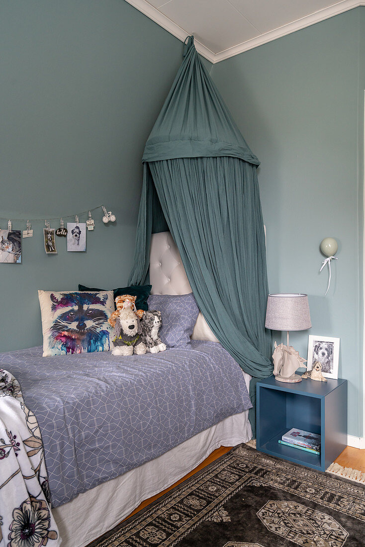 Bett mit Kuscheltieren und Betthimmel im Jungenzimmer mit graublauer Wand