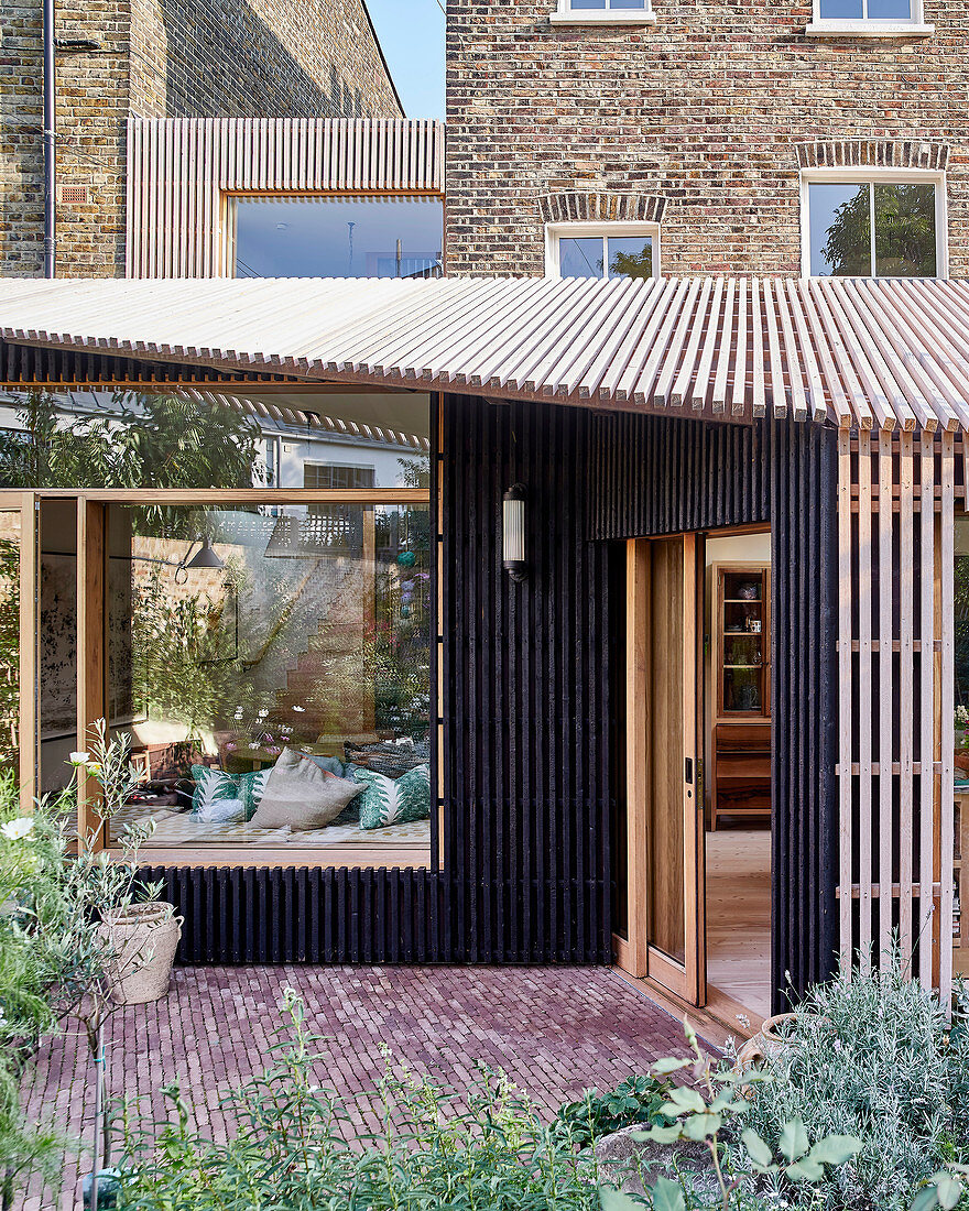 Modern extension with open façade structure made from wooden slats on brick house