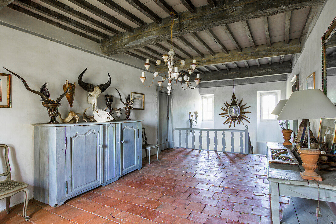 Collection of antlers and animal heads on landing with terracotta floor tiles and wood-beamed ceiling