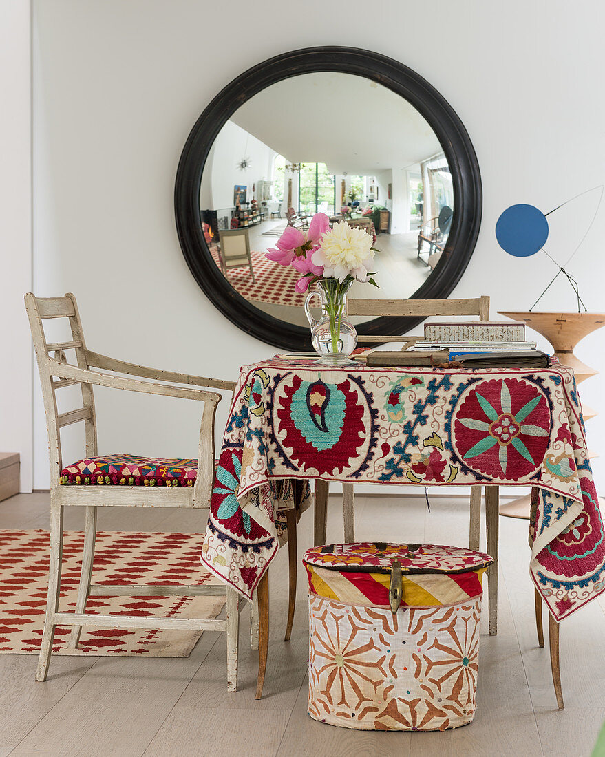 Großer konvexer Spiegel, davor Stuhl und Tisch mit alten Textilien