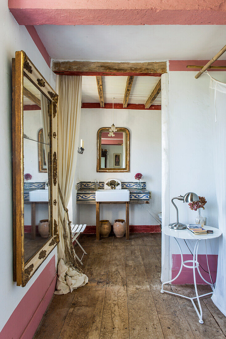 Mirror, side table and washbasin in bedroom with rustic wooden floorboards