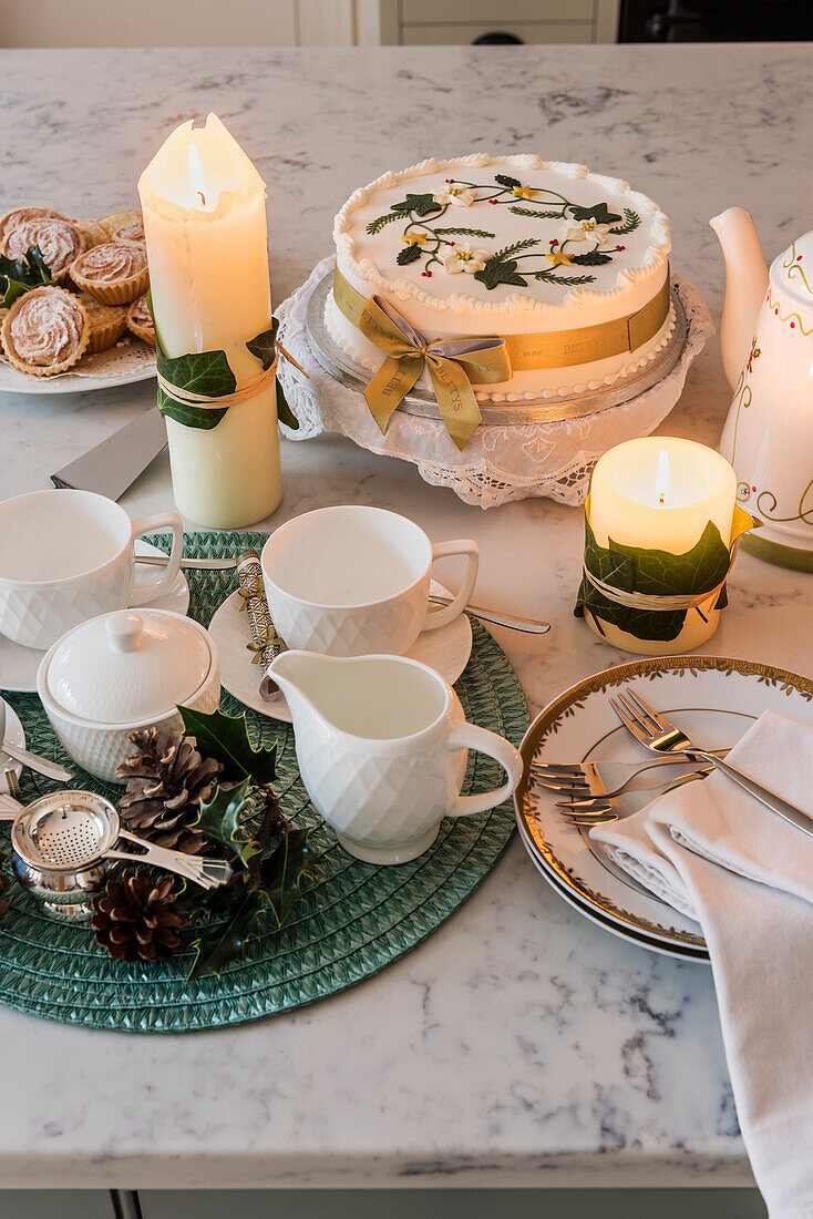 Weihnachtstorte, brennende Kerzen und Teeservice auf Marmorplatte