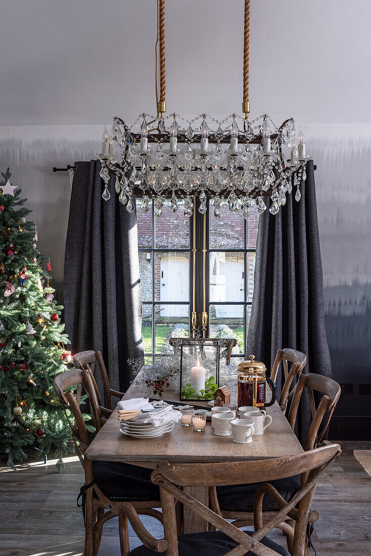 Rustikaler Holztisch mit Teeservice und Laterne, darüber Kronleuchter, Weihnachtsbaum in Zimmerecke