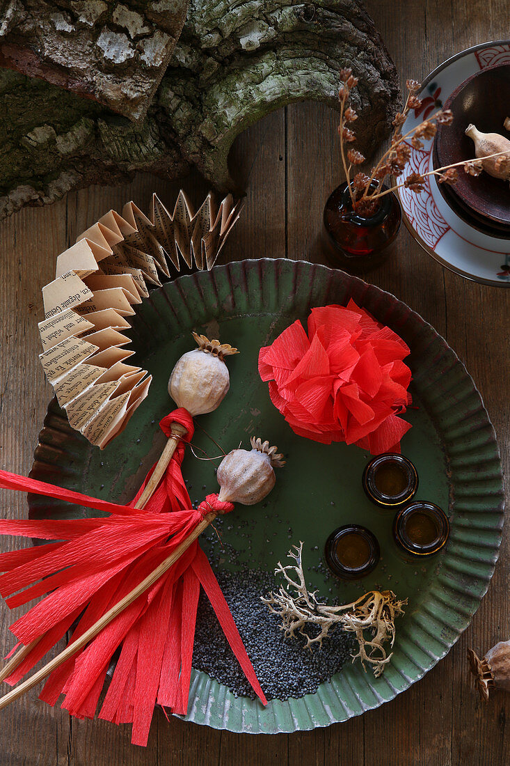 Dried poppy seed heads and red tassels on crepe paper