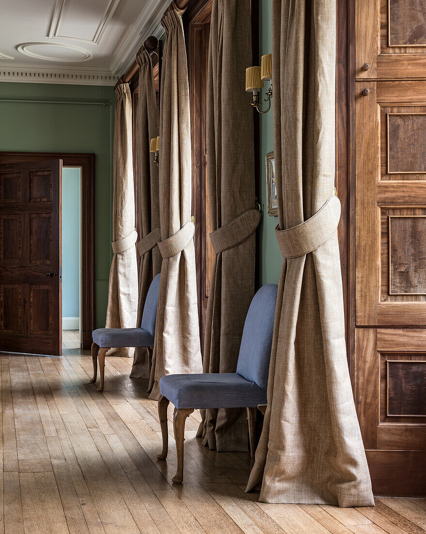 Upholstered chairs in the classic hallway with curtains at the window recesses
