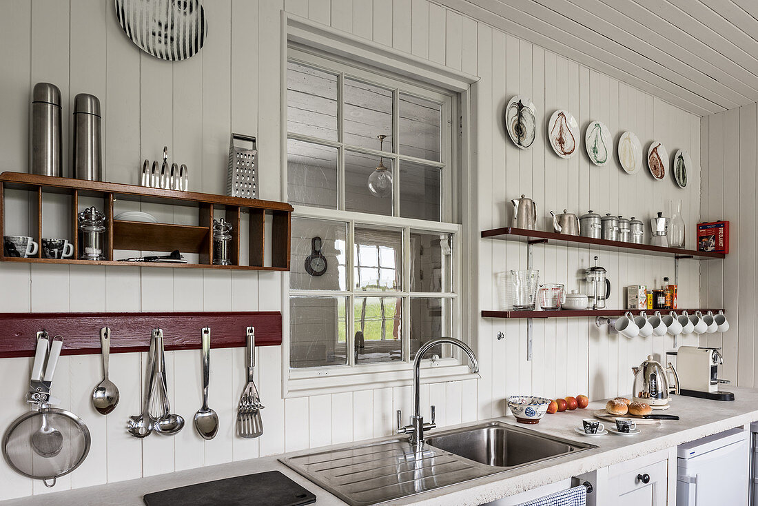 Kitchenware on shelves with stainless steel sink in 17th century stone cottage