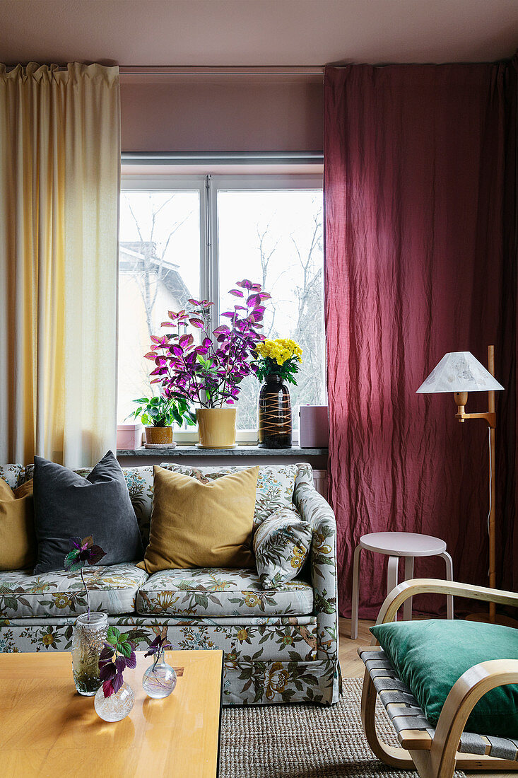 An upholstered sofa with a floral pattern in front of colourful curtains in a living room