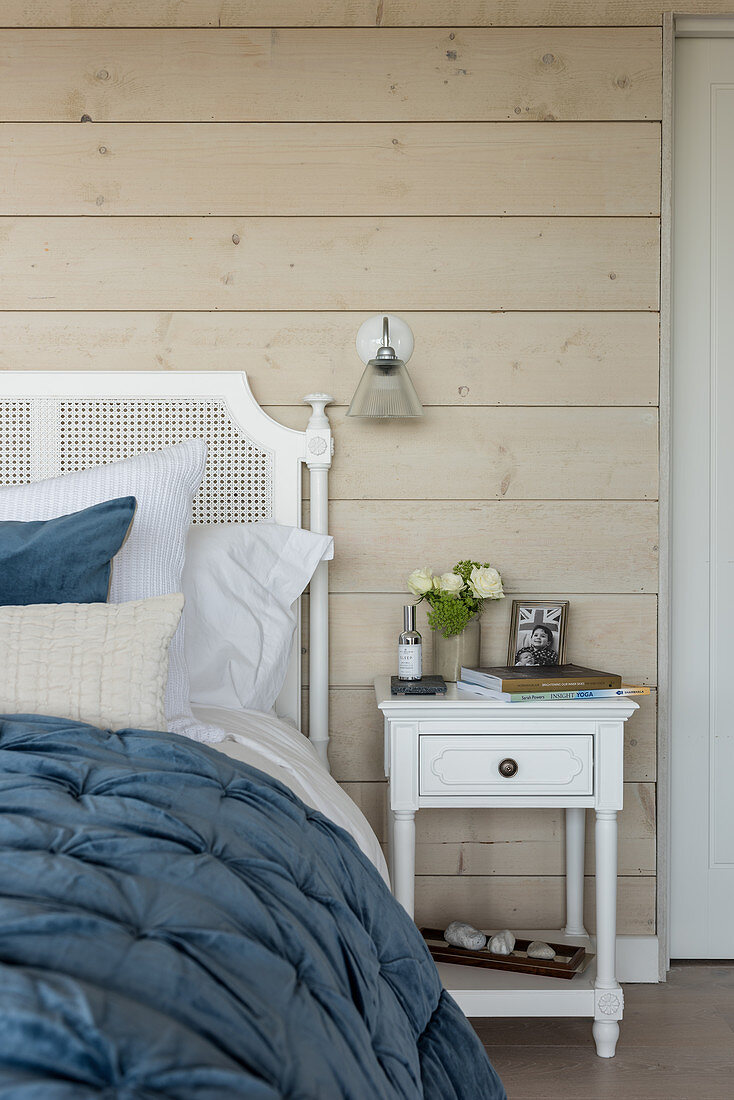 Blue quilt on double bed with wood cladding and glass wall light