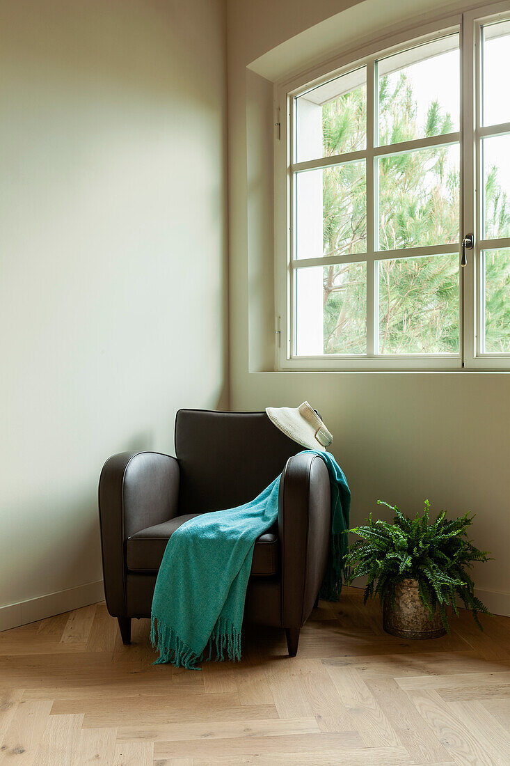 A leather armchair with a turquoise throw in the corner of a room