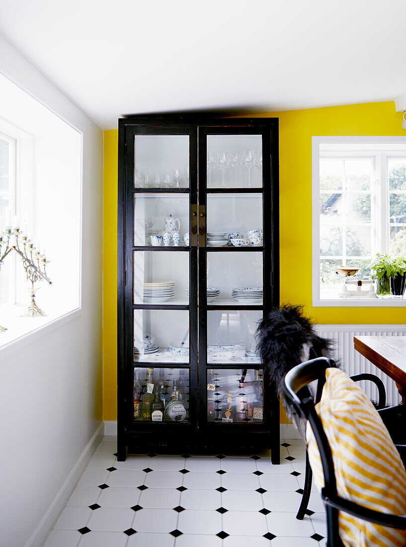 A crockery cabinet in front of a yellow wall in a dining room