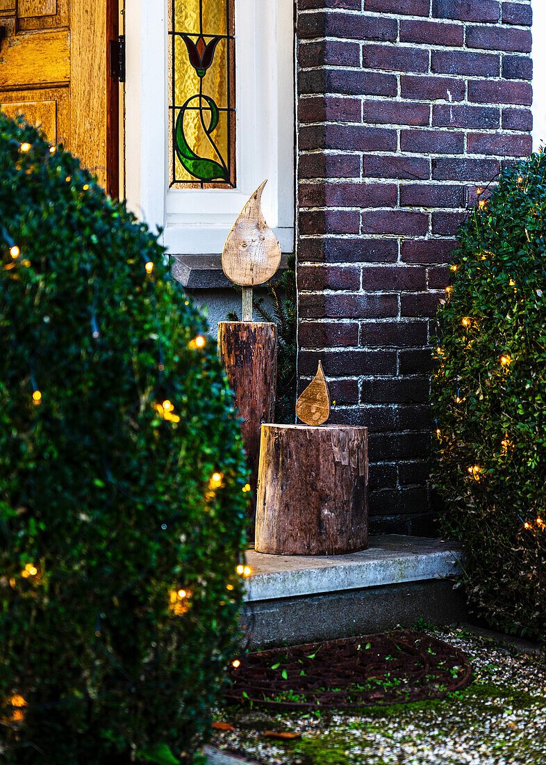 Decorative wooden sculptures in candle look at a Christmas-lit entrance to the house