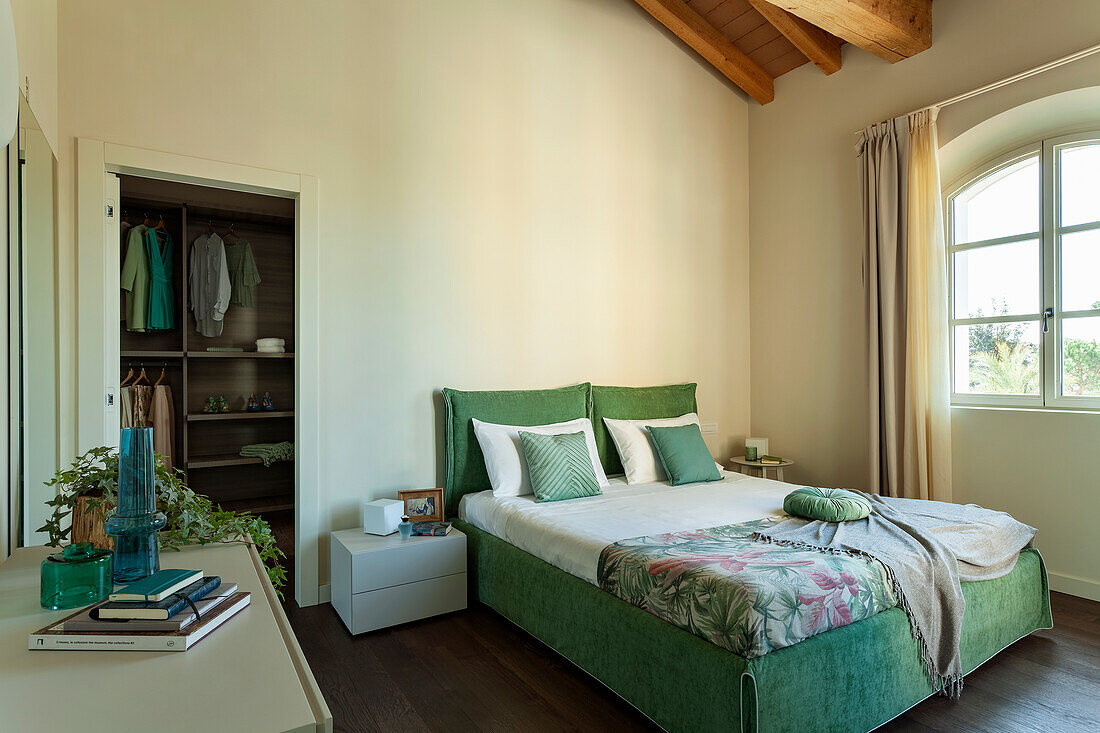 Doppelbett mit grünem Bezug und offener Kleiderschrank im Schlafzimmer