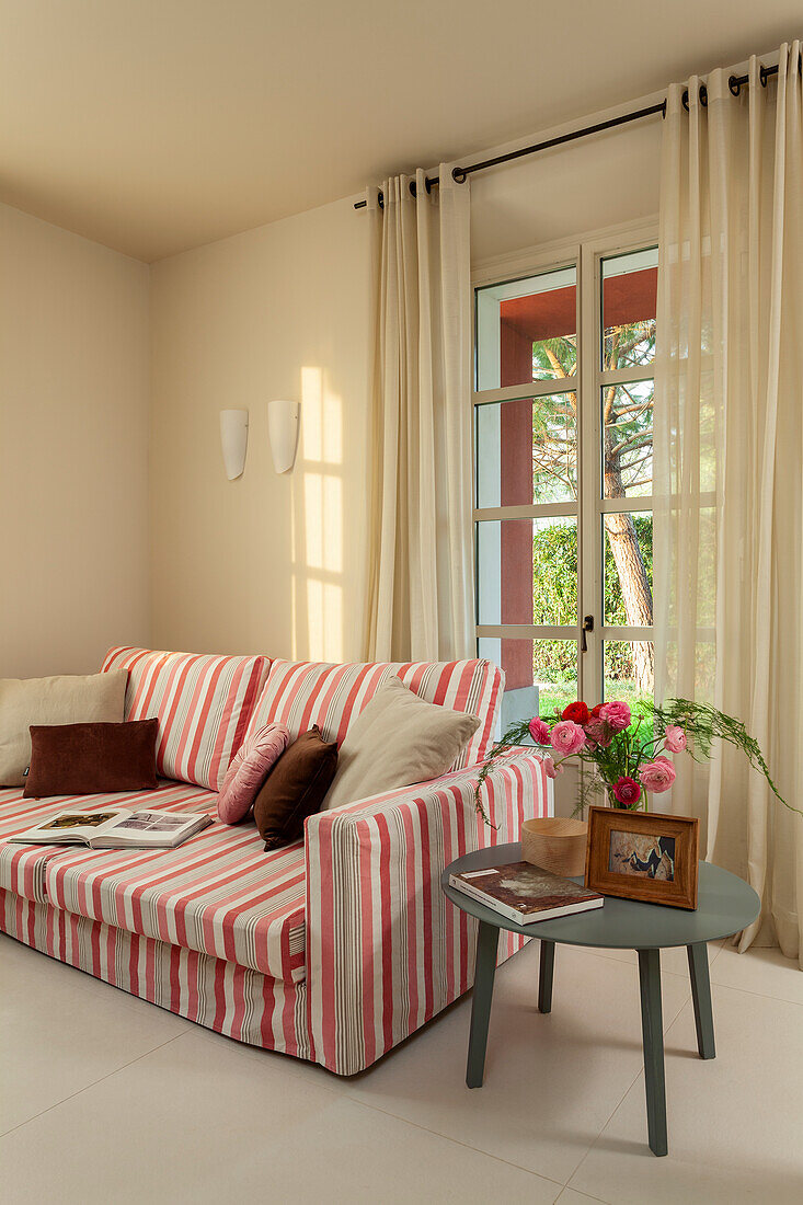 A sofa with striped upholstery and a side table in a living room with cream walls