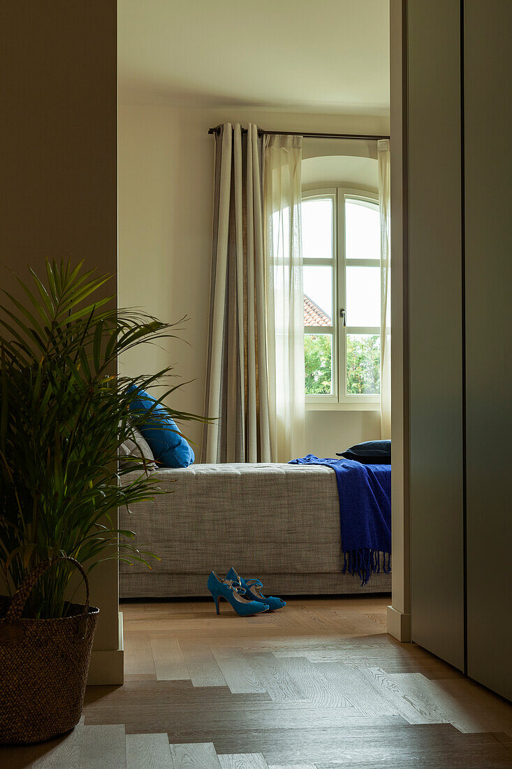 A view into a bedroom with a grey bedspread and a blue throw