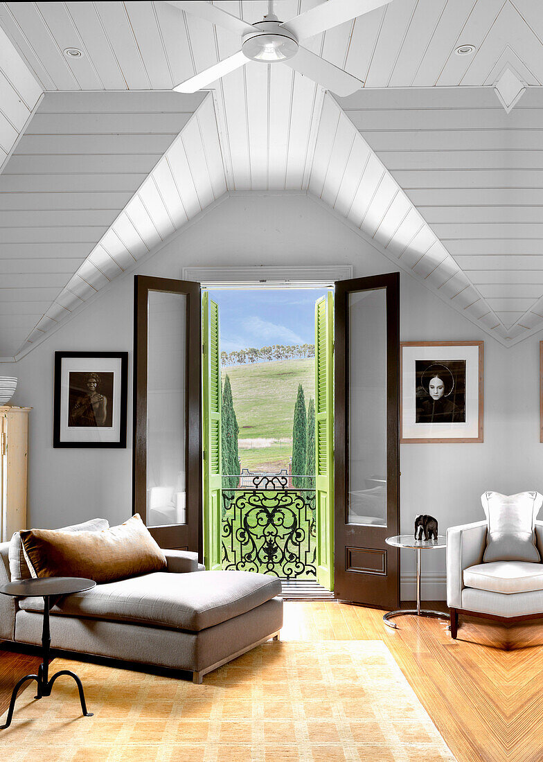 Chaiselongue, Sessel und Beistelltische im Zimmer mit weiß gestrichener Holzdecke und Balkon mit Landschaftsblick