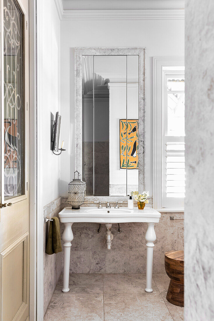 Waschtisch aus Keramik, darüber Spiegel im Badezimmer mit Marmorfliesen