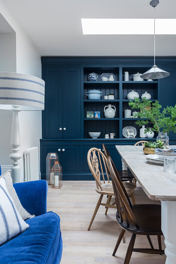 Long dining table with chairs and blue built in cupboard in the dining area with skylight