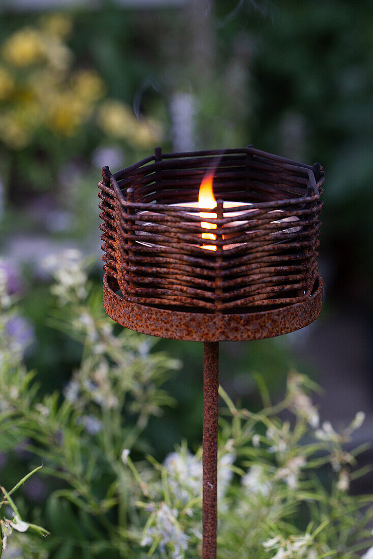 Rostiger Kerzenhalter mit brennender Kerze im garten