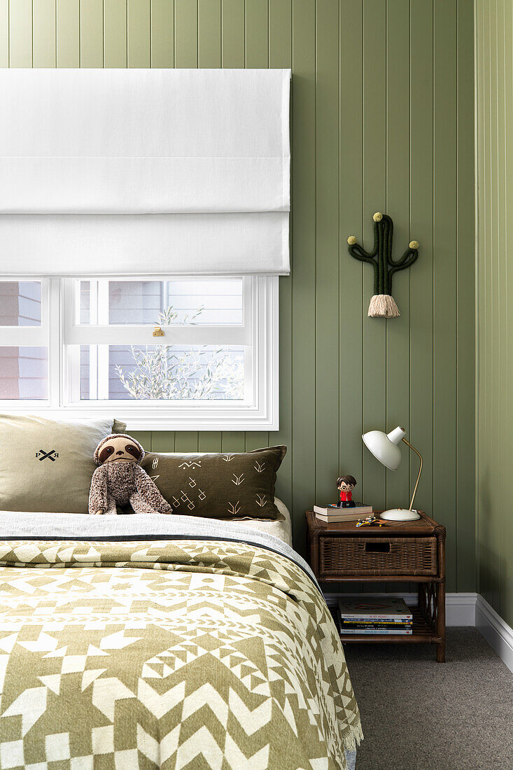 Double bed under window in bedroom with green painted wood paneled wall