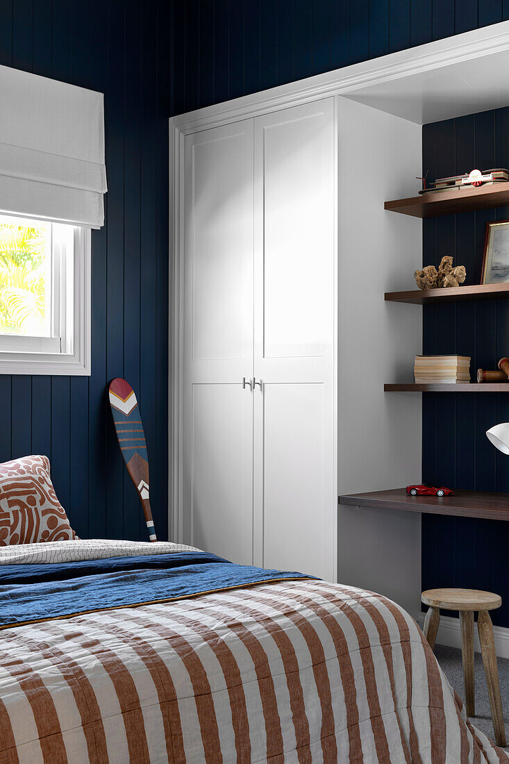 White built-in cabinet, shelves, and double bed in bedroom with dark blue beadboard wall