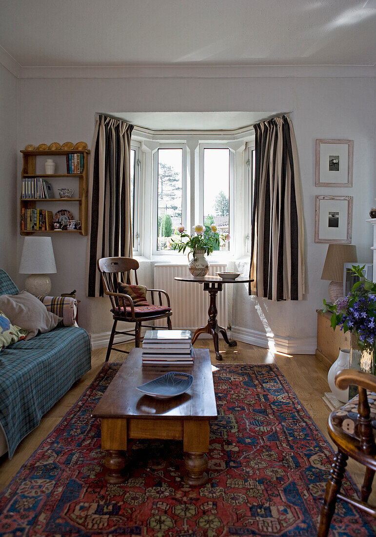 Alter Couchtisch aus Kiefernholz und gemusterter Teppich im  Wohnzimmer mit gestreiften Vorhängen