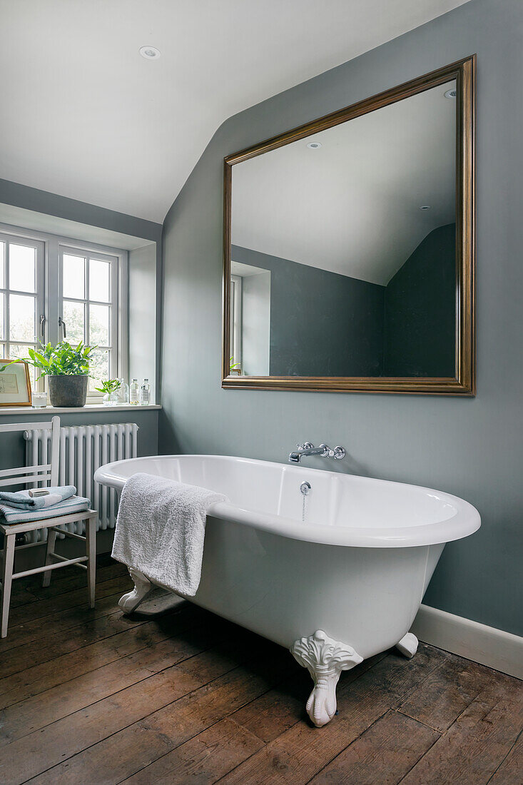 Überdimensionaler Spiegel an blau-grauer Wand über freistehender Badewanne