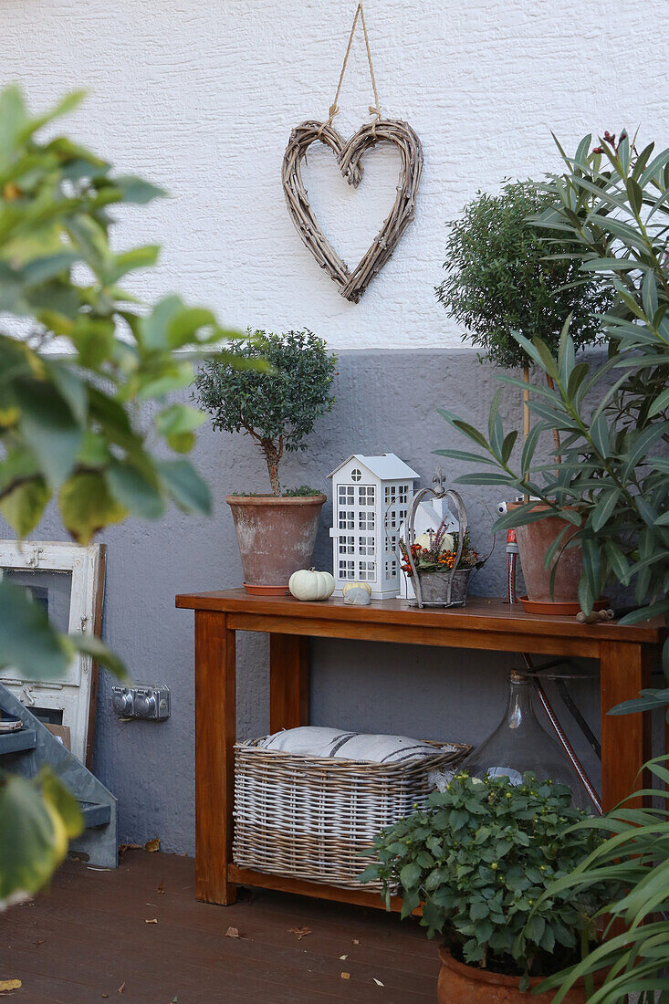 Konsolentisch mit Topfpflanzen und Windlicht, darüber Herzkranz an der Hauswand