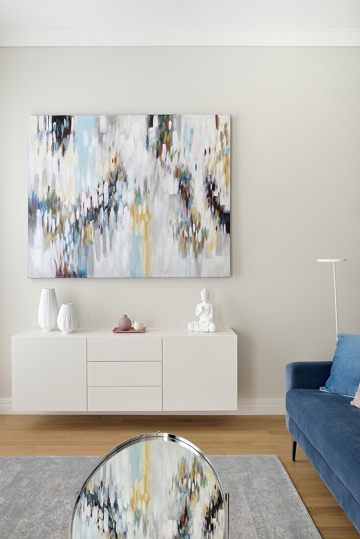 White sideboard, above it modern art in a bright living room