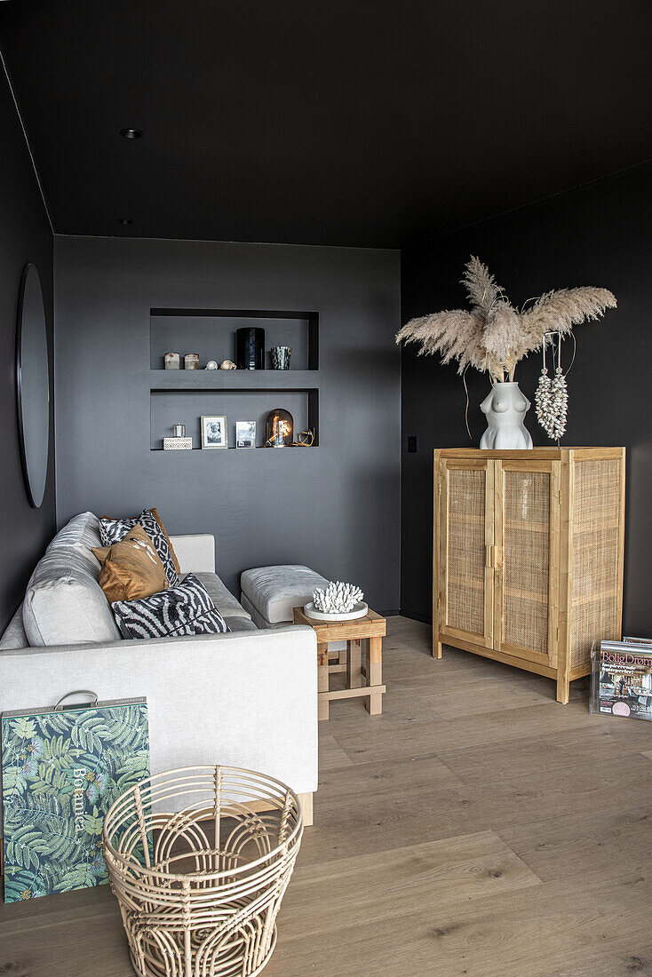 Light sofa with cushions and highboard in the living room with black walls