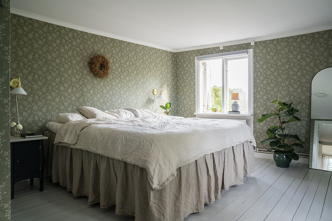 Double bed in a bedroom with floral wallpaper and light grey painted floorboards