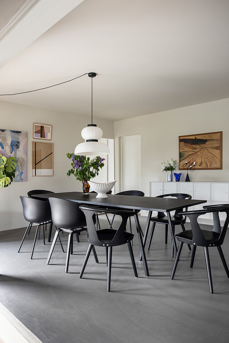 Black table, pendant lamp and designer chairs in dining room with concrete floor