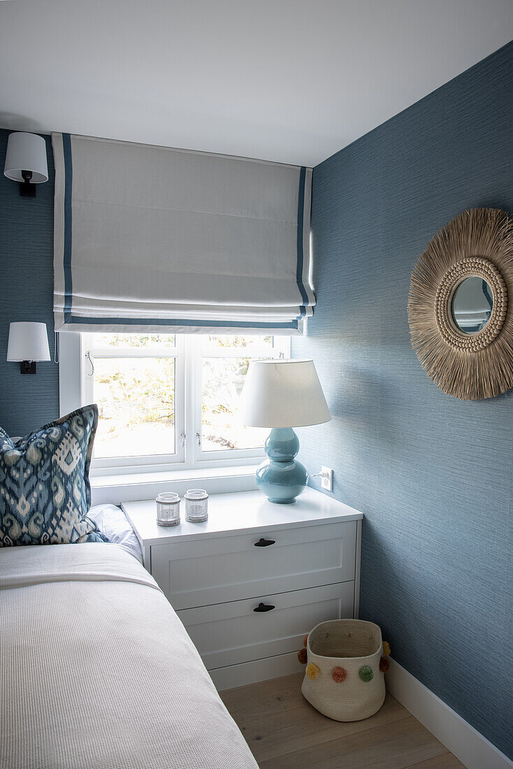 Bed and bedside cabinet in narrow room in blue and white tones