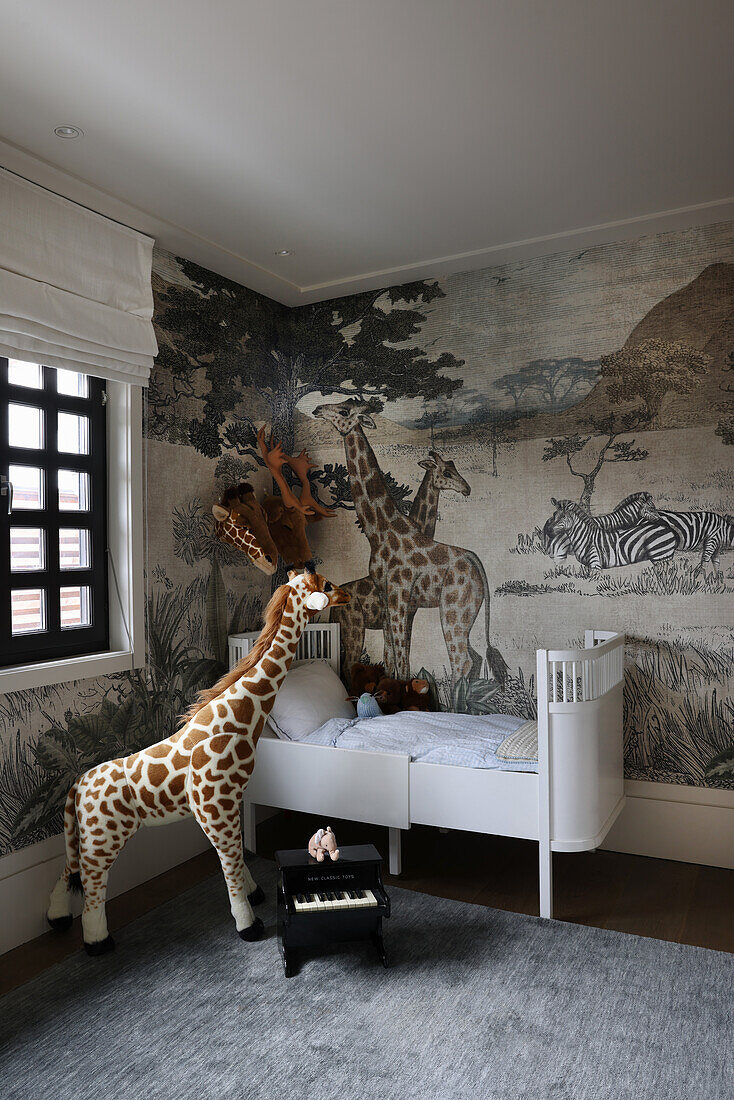 White child's bed and giraffe figure in front of wallpaper with national park motif