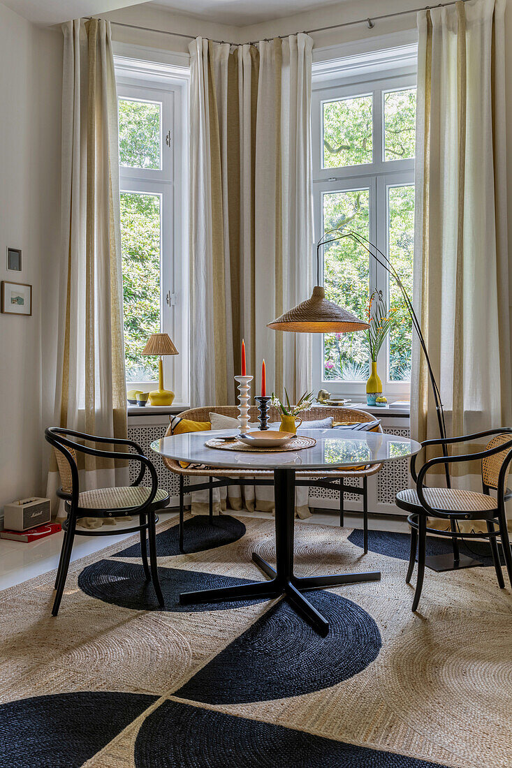 Round table with classic chairs in front of window in corner of room