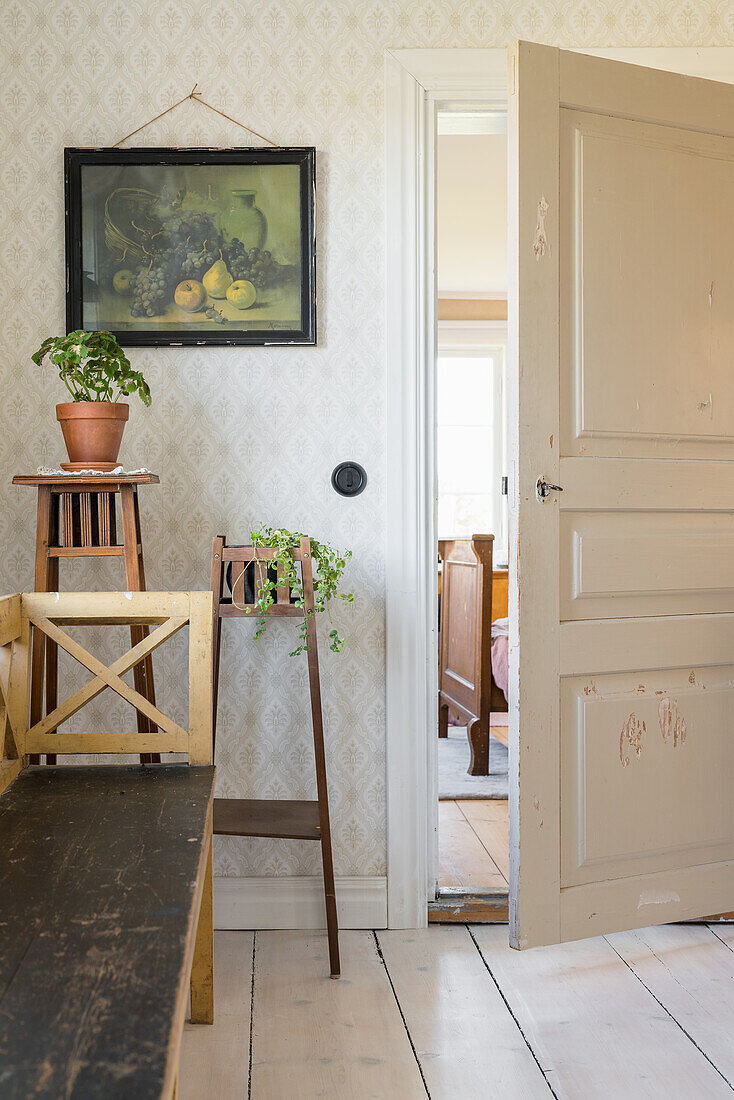 Long wooden bench, plant stand and painting in a hallway with wallpaper