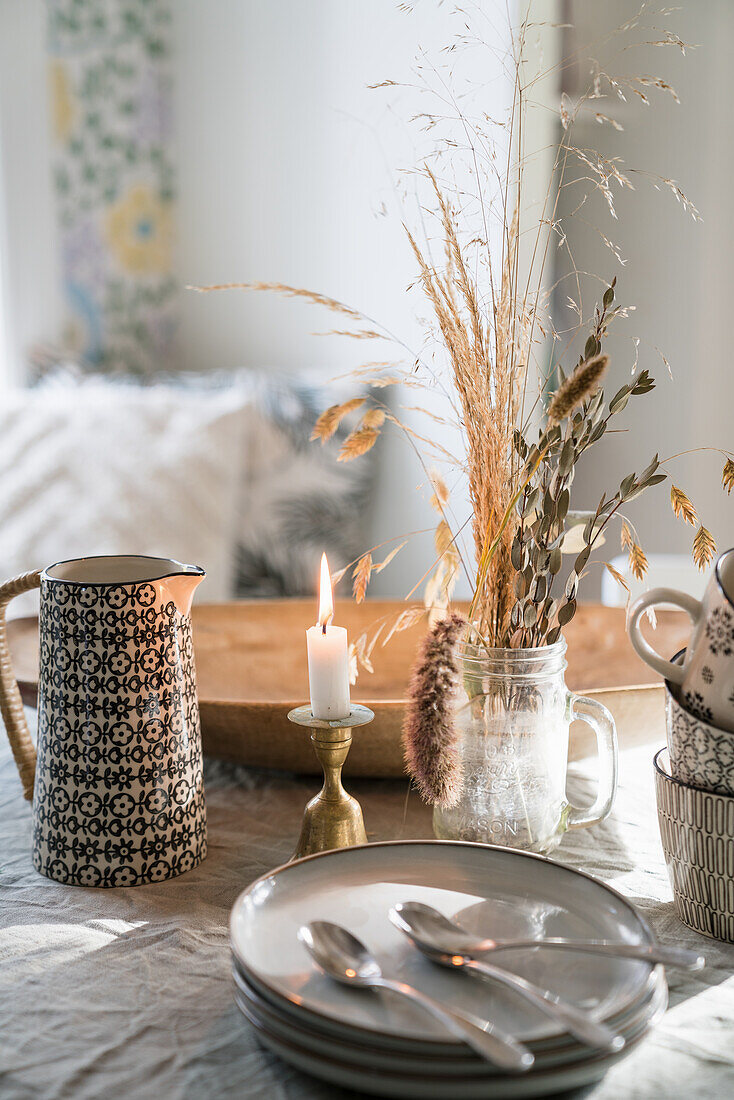 Autumnally decorated table with pile of plates, dried grasses, candle and pitcher