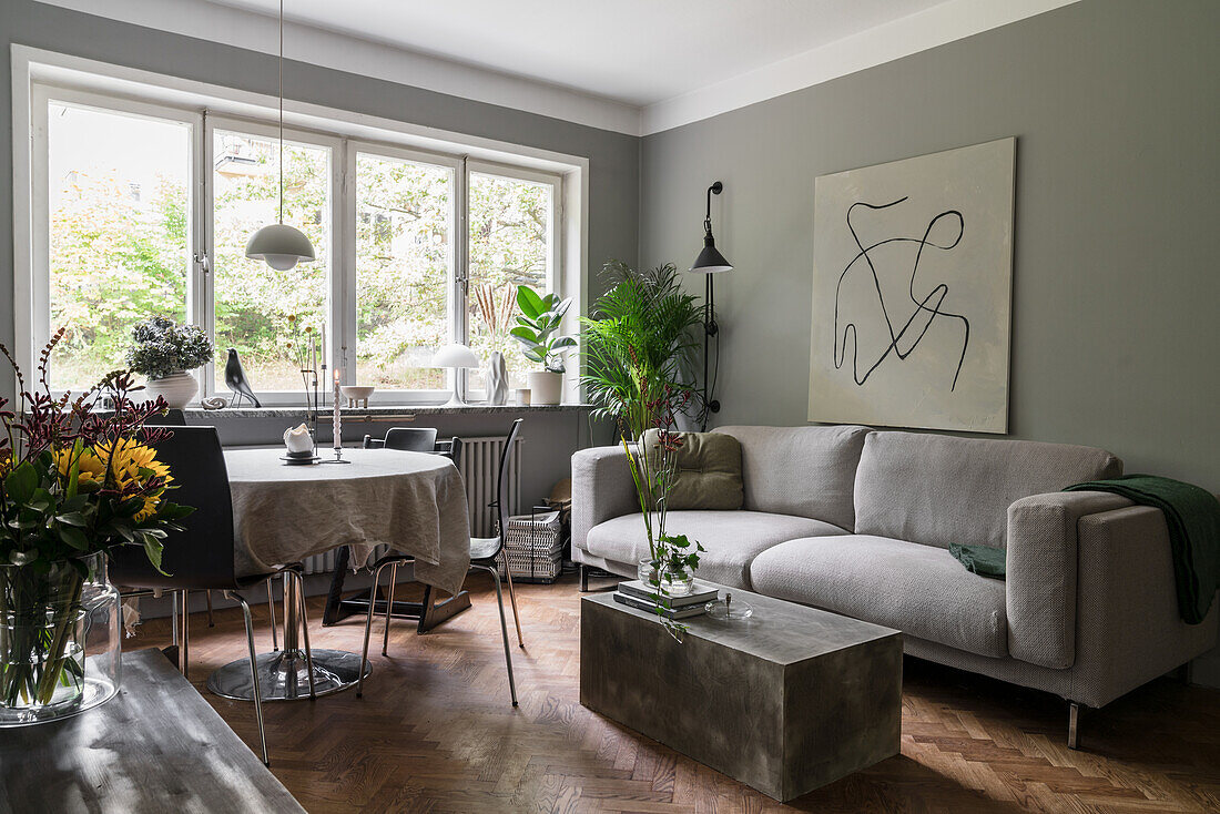 Grey upholstered sofa, concrete block as coffee table and dining area in front of window in open-plan living room