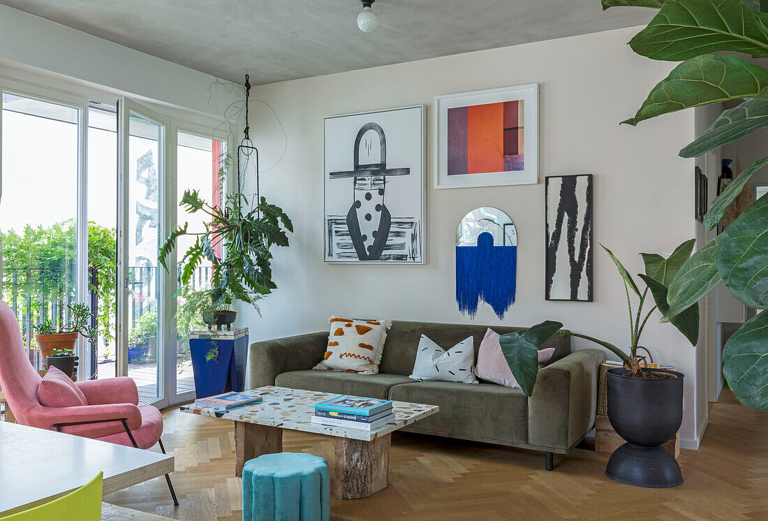 Seating area with sofa, modern artwork and houseplants in front of patio door in open-plan living room