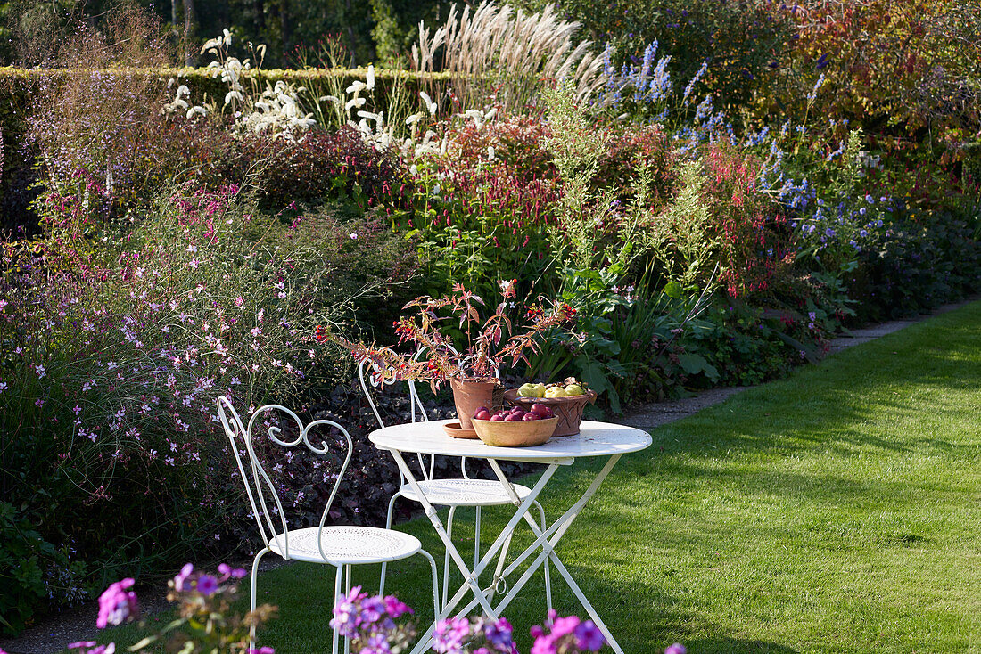 Gartentisch mit Stühlen auf Rasen vor Staudenbeet im sommerlichen Garten