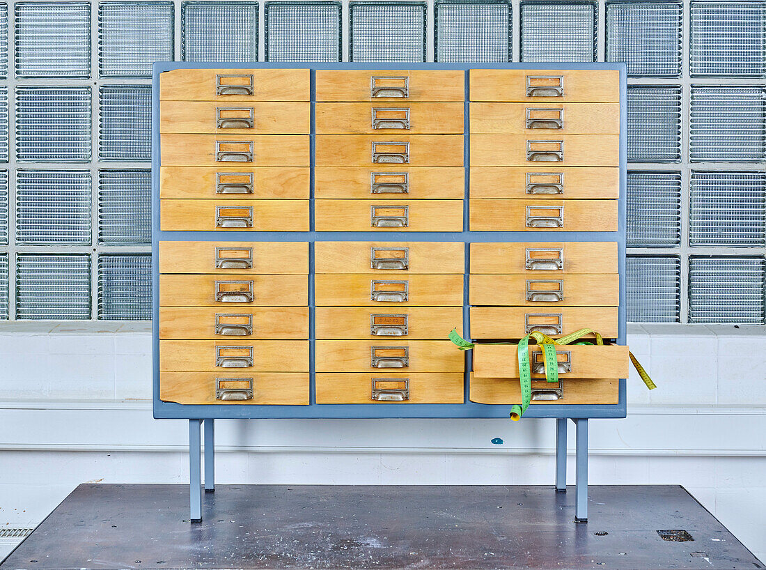 Schrank im Industrial-Design mit Holzschubladen und Maßband, Glasbausteinwand